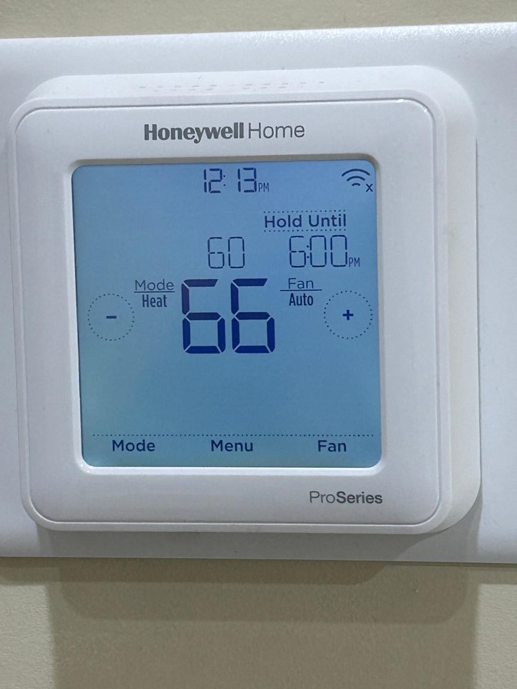 White Honeywell Home digital thermostat displaying heat mode on a wall.