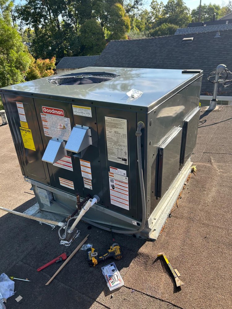 Gray Goodman packaged HVAC unit on a roof with visible connections and tools nearby.