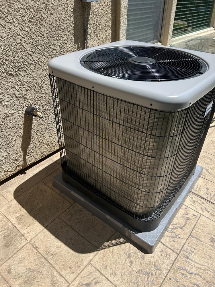 Outdoor air-conditioning unit with a top fan beside a stucco wall and patio.