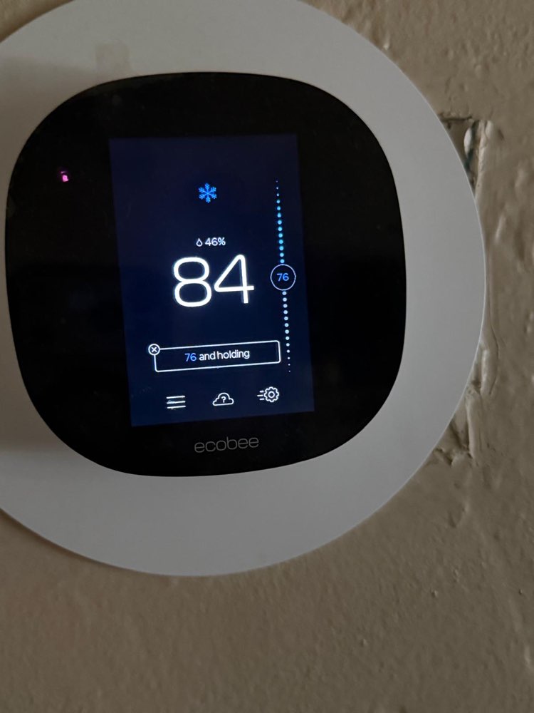 Black ecobee smart thermostat with a white backing plate mounted on a wall.
