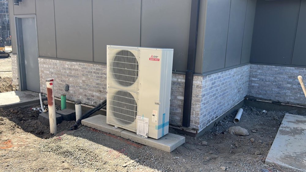 Tall Mitsubishi Electric outdoor HVAC unit with two fans on a concrete base beside a building.