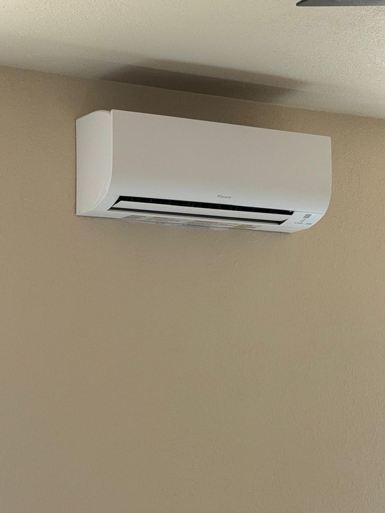 White Daikin mini-split indoor unit mounted high on a beige wall.