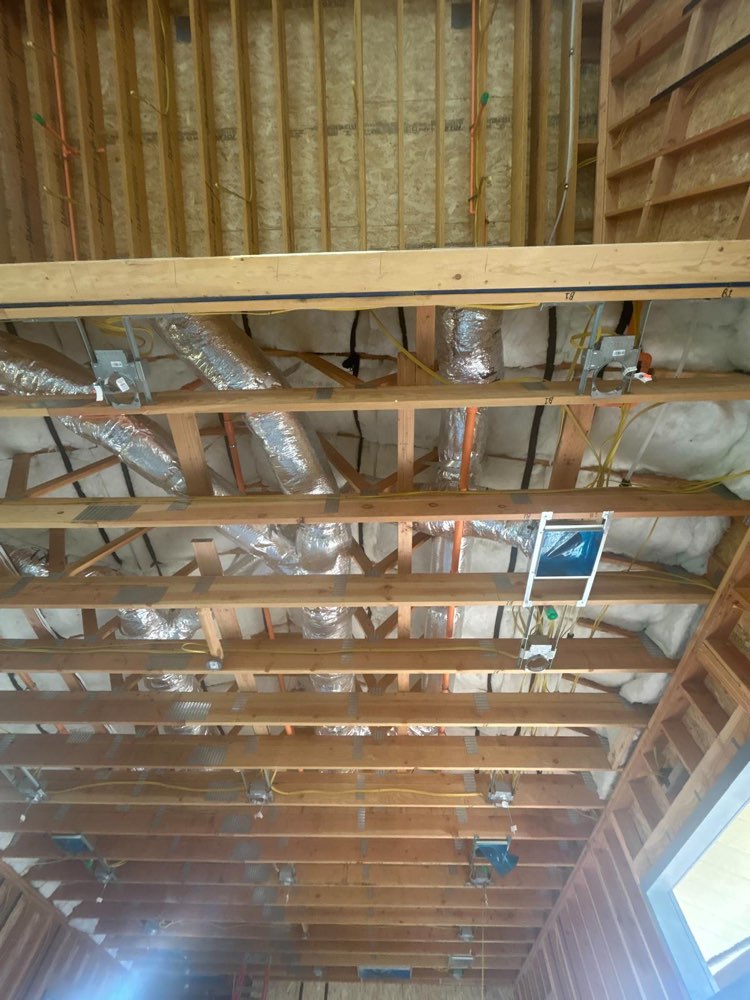 Insulated flexible air ducts routed through exposed wood ceiling framing.