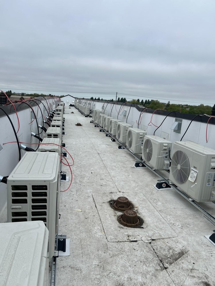 Two long rows of compact outdoor HVAC units on a flat roof with visible connecting lines.