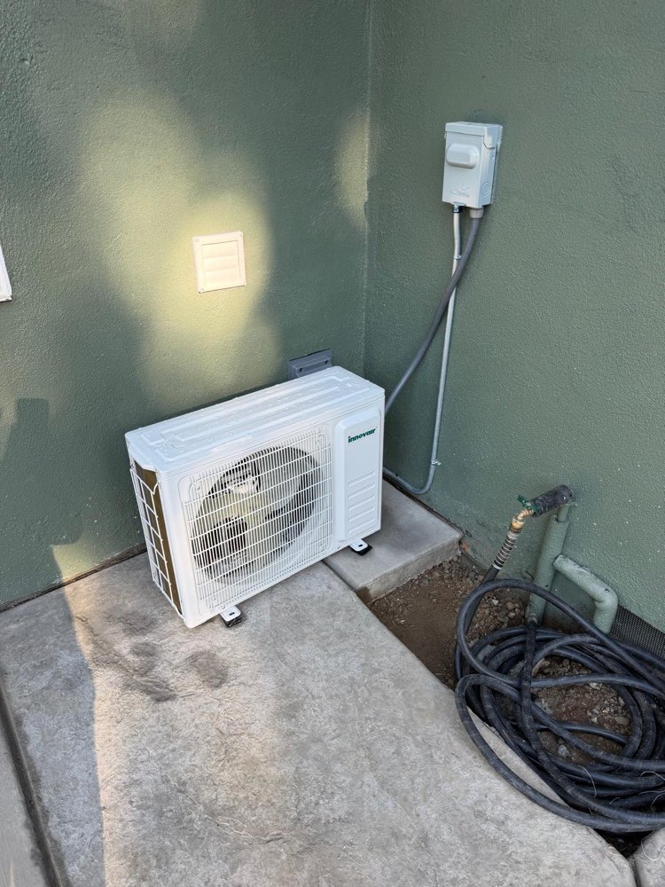 White Innovair outdoor mini-split unit on concrete beside a green stucco wall.