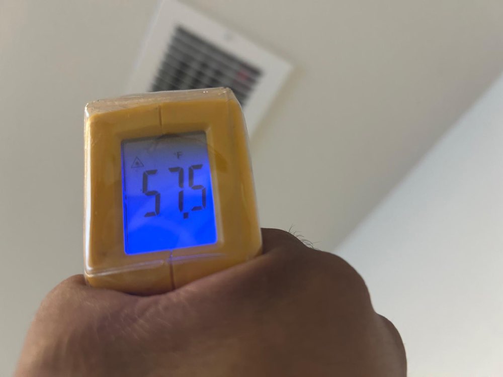 Handheld infrared thermometer displaying 57.5°F with a ceiling air grille in the background.