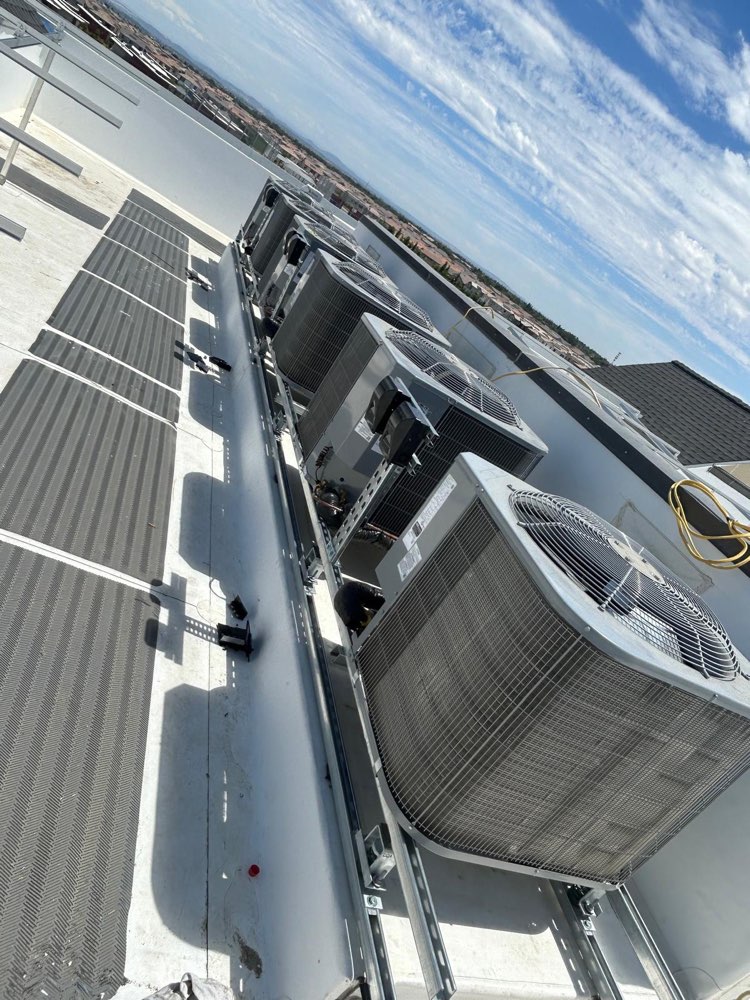 A row of outdoor air-conditioning units with top fans on rooftop support rails.